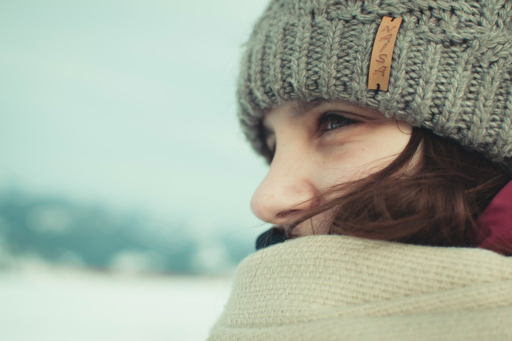 Woman wearing a knitted winter hat and scarf looking into the snowy landscape.