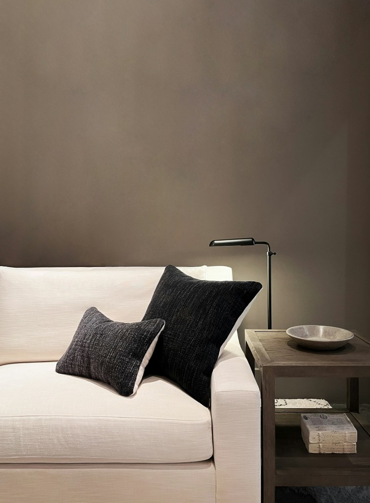 Minimalist living room with a cream sofa, black throw pillows, and a simple wooden side table against a neutral wall.