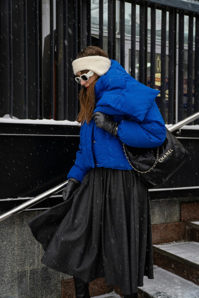 woman wearing a blue puffer jacket with a skirt and winter accessories in snowy weather