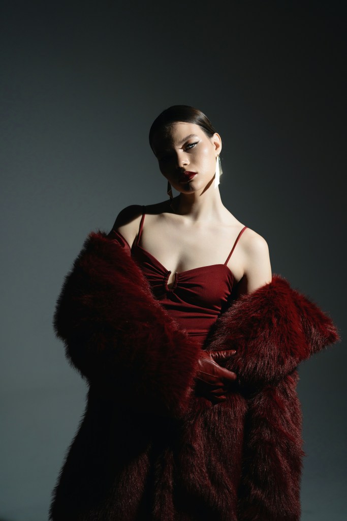 Model wearing a burgundy dress with a faux fur coat, showcasing luxury winter fashion 2025 eveningwear.