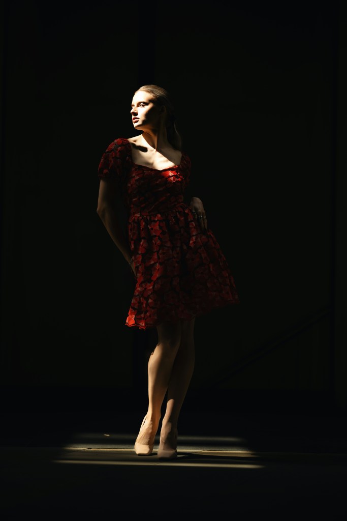 Model in a red lace cocktail dress under spotlight, representing bold red winter party fashion.