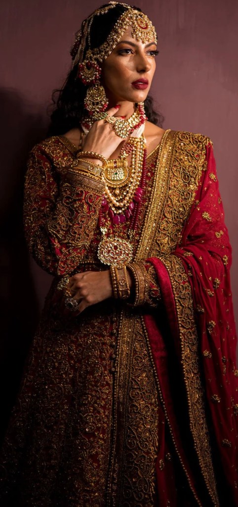 Close-up of red Mughal bridal dress showcasing intricate stone work and traditional gold accessories.