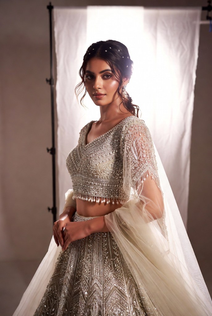 Silver bridal lehenga with intricate beadwork and a detachable sheer tulle overskirt, styled in a modern high-fashion bridal editorial.